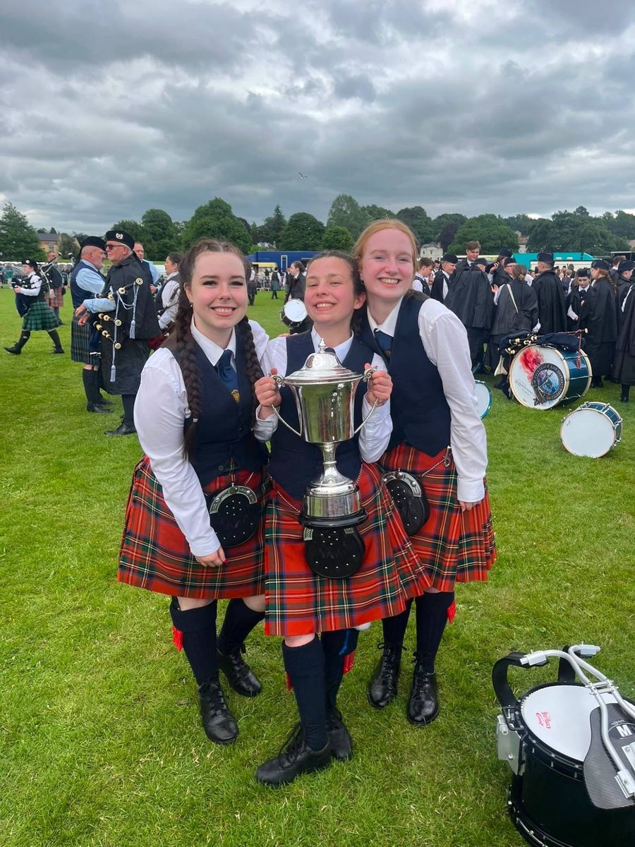 Three young band members in uniform celebrating with a silver trophy