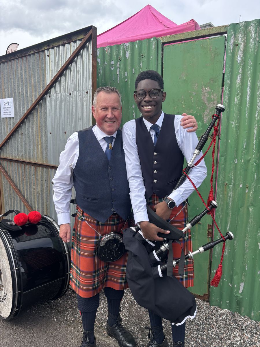 A smiling band member with a young piper holding his bagpipes