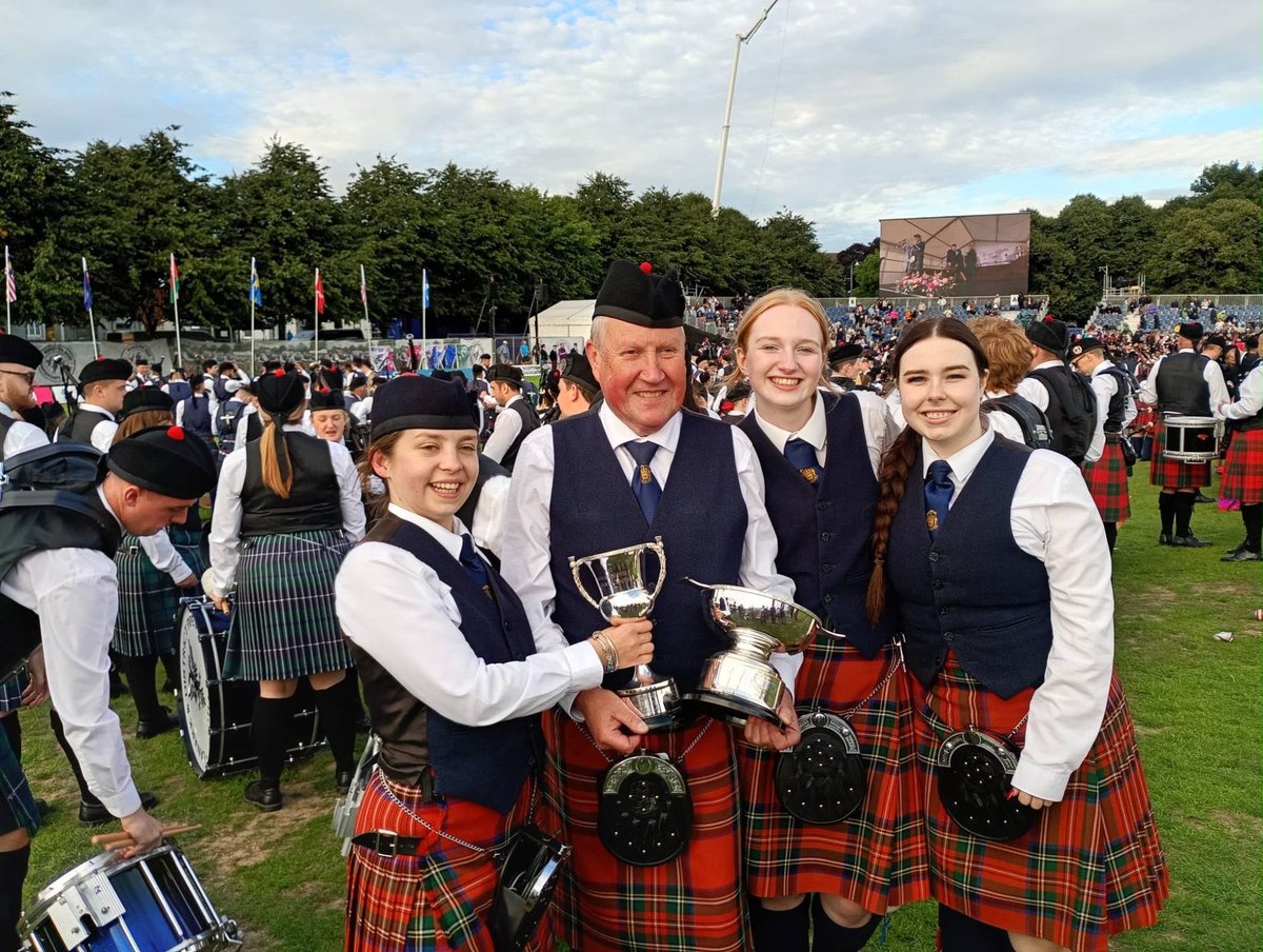 Four band members holding trophies at Glasgow Green after the World Pipe Band Championships